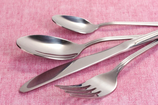 Vidlička, lžíce a nůž na růžové ubrus — Stock fotografie