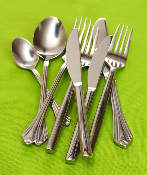Vorken, lepels en messen op een groene tafellaken — Stockfoto