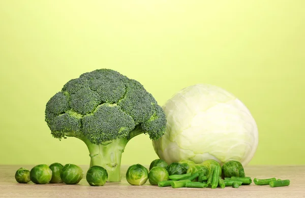 Fresh broccoli and cabbages on wooden table on green background — Stock Photo, Image