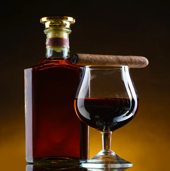 Бутылка и стакан бренди и сигары на коричневом фоне — стоковое фото