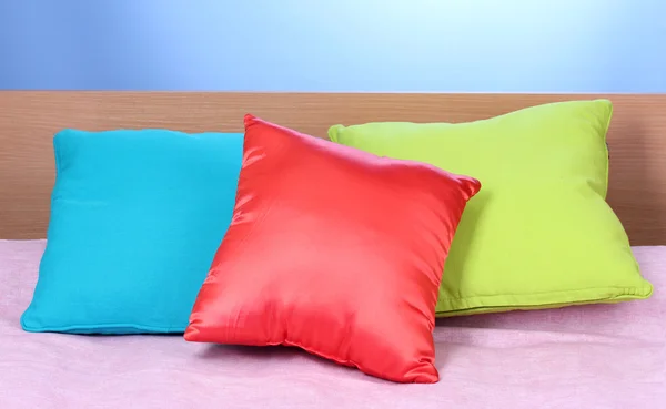 Almofadas brilhantes na cama no fundo azul — Fotografia de Stock