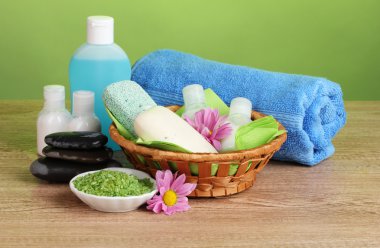 Hotel amenities kit in basket on wooden table on green background clipart