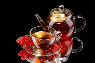 Glass teapot and cup with black viburnum tea isolated on black clipart