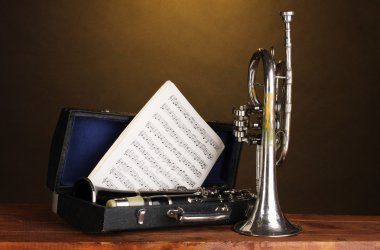 Antique trumpet and clarinet in case on wooden table on brown background clipart