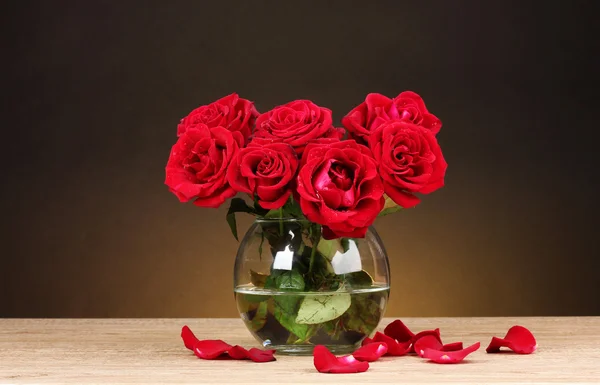 Красивые красные розы в вазе на деревянном столе на коричневом фоне — стоковое фото