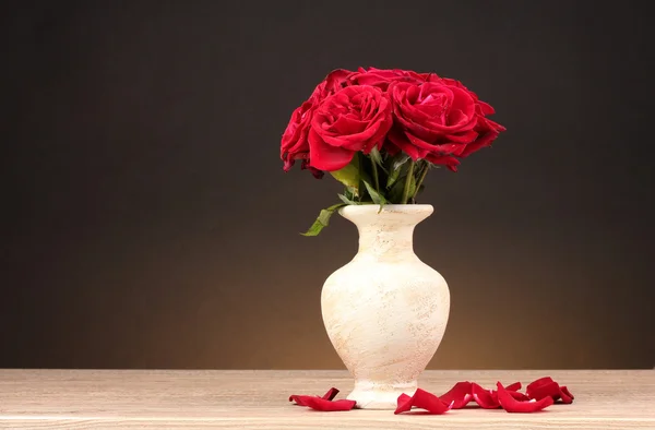 Schöne rote Rosen in Vase auf Holztisch auf braunem Hintergrund — Stockfoto