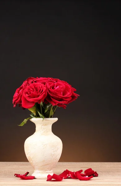 茶色の背景に木製のテーブルの上の花瓶に美しい赤いバラ — ストック写真