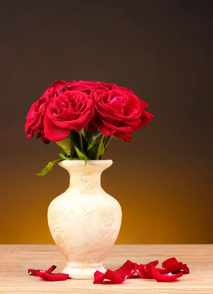Vackra röda rosor i vas på träbord på brun bakgrund — Stockfoto