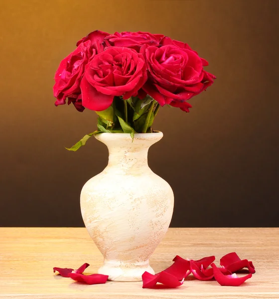 茶色の背景に木製のテーブルの上の花瓶に美しい赤いバラ — ストック写真