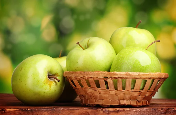 Manzanas verdes jugosas en cesta sobre mesa de madera sobre fondo verde —  Fotos de Stock