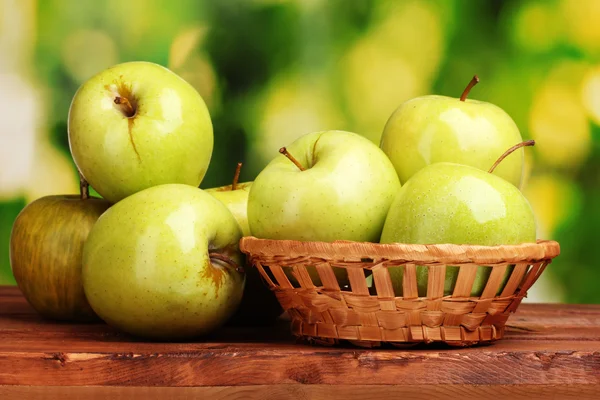 Soczyste zielone jabłka kosz na drewnianym stole na zielonym tle — Zdjęcie stockowe