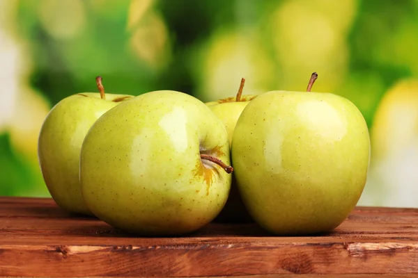 Saftige grüne Äpfel auf Holztisch auf grünem Hintergrund — Stockfoto