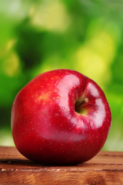 Soczyste czerwone jabłko na drewnianym stole na zielonym tle — Zdjęcie stockowe