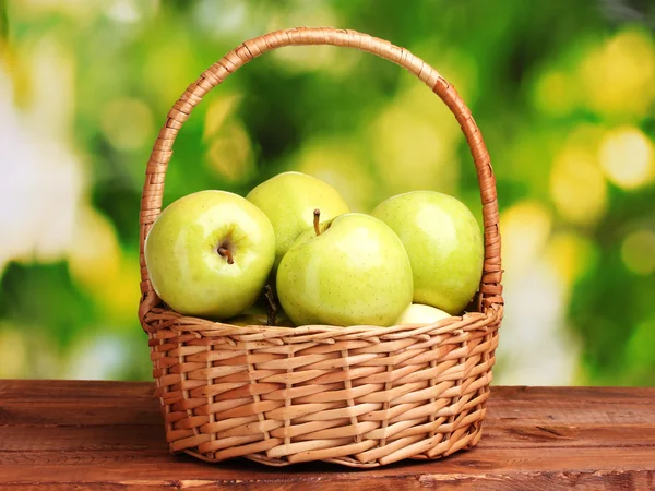 Manzanas verdes jugosas en cesta sobre mesa de madera sobre fondo verde — Foto de Stock