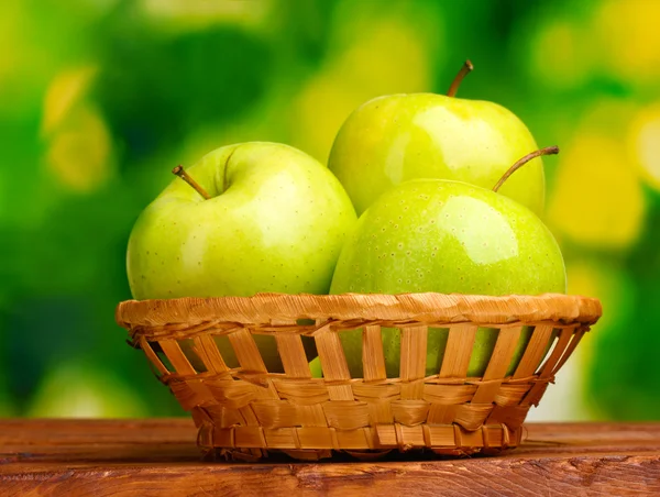 Saftige grüne Äpfel im Korb auf Holztisch auf grünem Hintergrund — Stockfoto