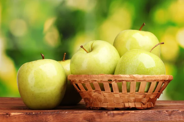 Manzanas verdes jugosas en cesta sobre mesa de madera sobre fondo verde —  Fotos de Stock