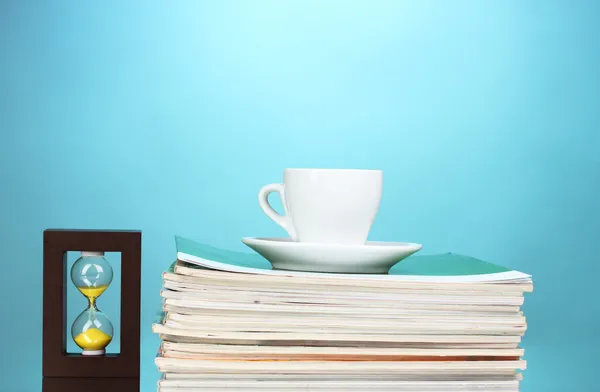 Stack av tidskrifter, cup och timglas på blå bakgrund — Stockfoto