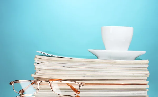 Stapel tijdschriften, cup en bril op blauwe achtergrond — Stockfoto