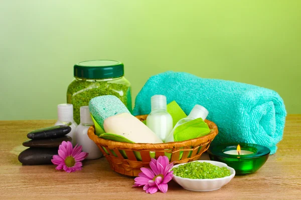 Hotel amenities kit in basket on wooden table on green background — Stock Photo, Image