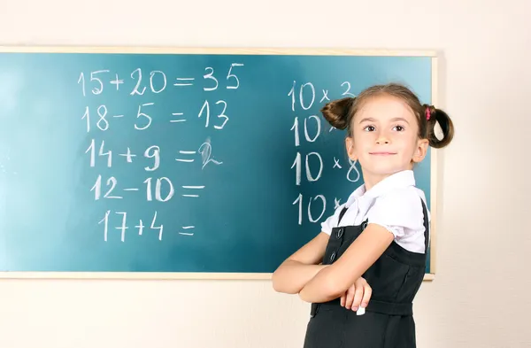Linda menina de pé perto de quadro negro na sala de aula — Fotografia de Stock