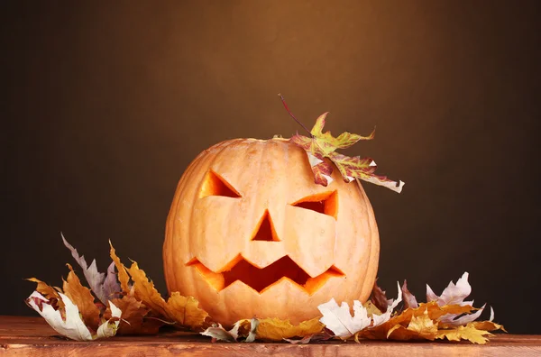 Calabaza de Halloween y hojas de otoño sobre mesa de madera sobre fondo marrón —  Fotos de Stock