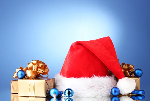 Hermoso sombrero de Navidad, regalos y bolas de Navidad sobre fondo azul —  Fotos de Stock