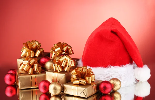 Bonito chapéu de Natal, presentes e bolas de Natal no fundo vermelho — Fotografia de Stock