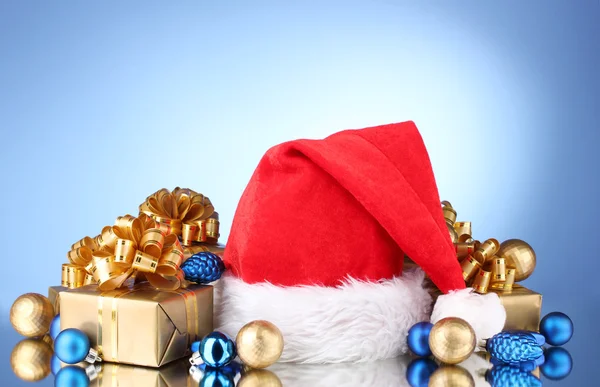 Hermoso sombrero de Navidad, regalos y bolas de Navidad sobre fondo azul — Foto de Stock