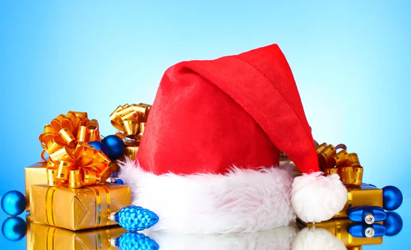 Hermoso sombrero de Navidad, regalos y bolas de Navidad sobre fondo azul —  Fotos de Stock