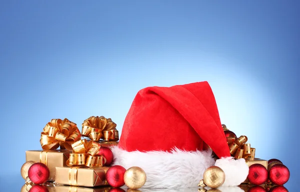 Schöne Weihnachtsmütze, Geschenke und Weihnachtskugeln auf blauem Hintergrund — Stockfoto