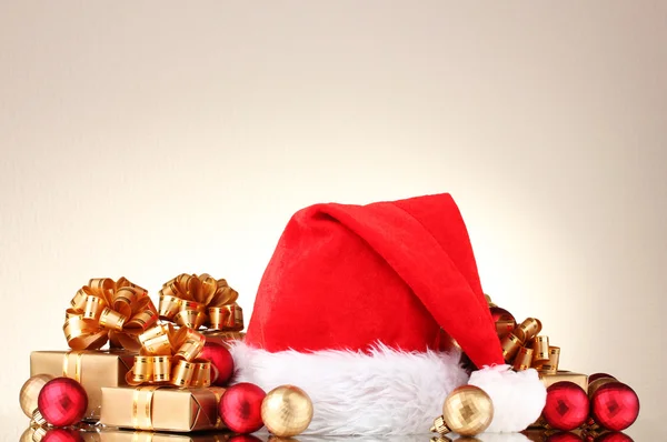 Krásné vánoční čepici, dárky a vánoční koule na šedém pozadí — Stock fotografie