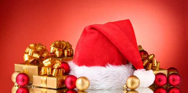 Hermoso sombrero de Navidad, regalos y bolas de Navidad sobre fondo rojo — Foto de Stock