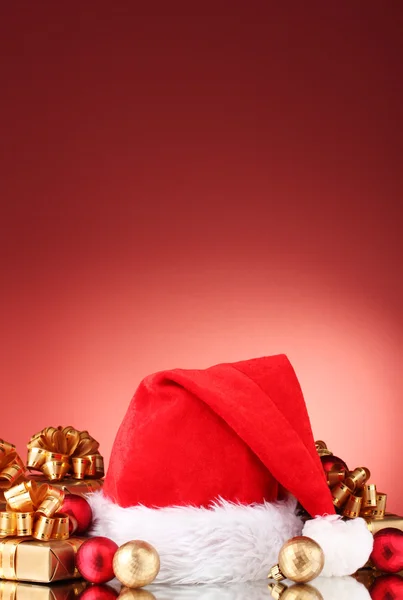 Bonito chapéu de Natal, presentes e bolas de Natal no fundo vermelho — Fotografia de Stock