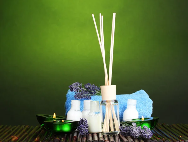 Освежитель воздуха, бутылки, полотенце и свечи на бамбуковом коврике на зеленом фоне — стоковое фото