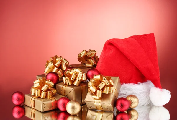 Güzel Noel şapka, hediye ve kırmızı bir arka plan üzerinde Noel topları — Stok fotoğraf