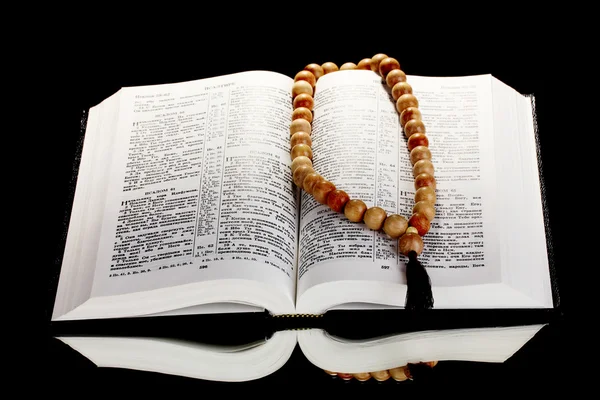 Sacra Bibbia russa aperta con rosario in legno su sfondo nero — Foto Stock