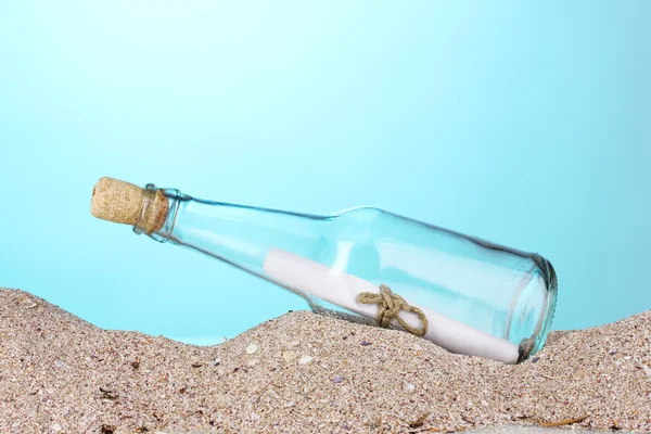 Glass bottle with note inside on sand on blue background — Stockfoto