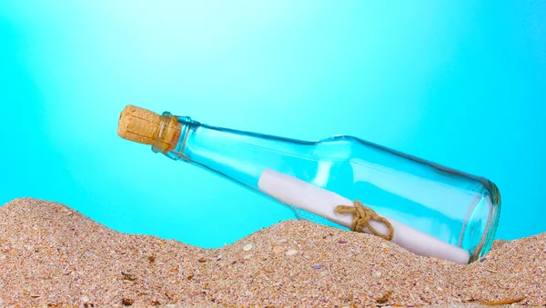 Garrafa de vidro com nota dentro na areia no fundo azul — Fotografia de Stock