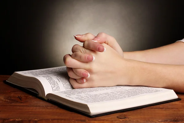 Hände im Gebet über offener russischer Heiliger Bibel auf schwarzem Hintergrund gefaltet — Stockfoto