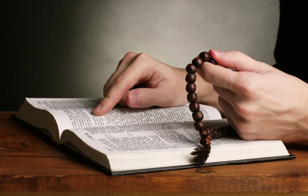 Händerna hålla trä Rosenkransen över öppna ryska Bibeln på grå bakgrund — Stockfoto