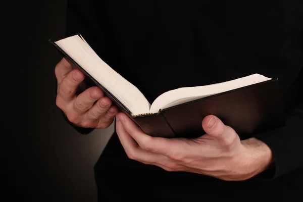 Mains tenant ouverte la bible russe sur fond noir — Photo