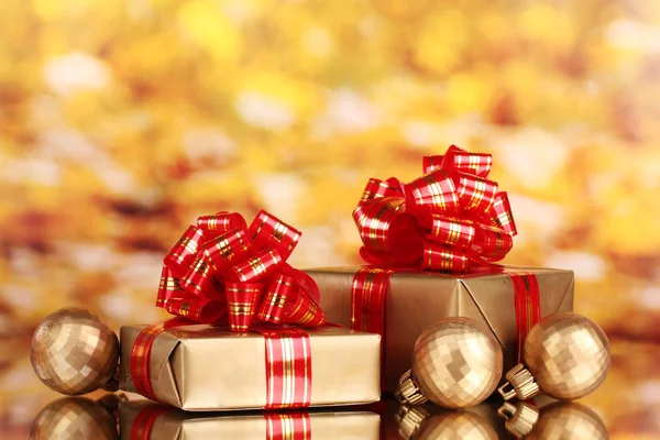 Mooie gouden geschenken met rood lint en kerstballen op gele backgr — Stockfoto