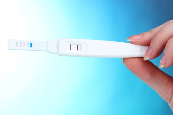 Schwangerschaftstest in der Hand auf blauem Hintergrund — Stockfoto
