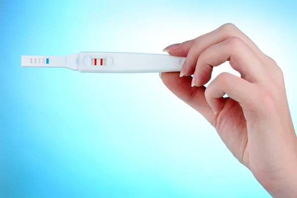 Teste de gravidez na mão sobre fundo azul — Fotografia de Stock