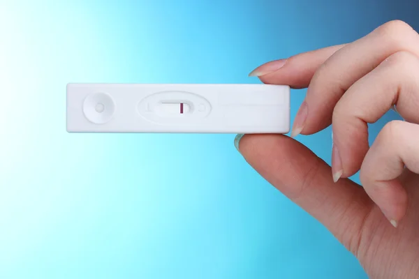 Prueba de embarazo en la mano sobre fondo azul — Foto de Stock
