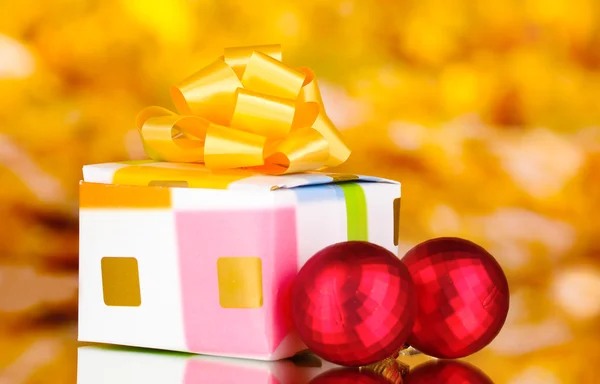 Kerstballen en gift op gele achtergrond — Stockfoto