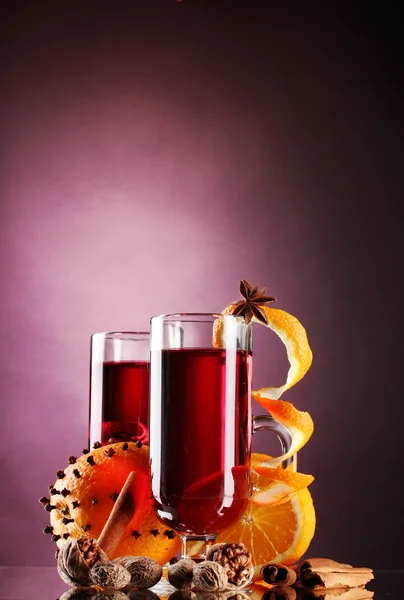 Vinho quente nos copos, tempero e laranja no fundo roxo — Fotografia de Stock
