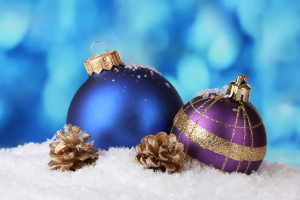 Красиві блакитні і фіолетові різдвяні кульки і шишки в снігу на синьому фоні — стокове фото
