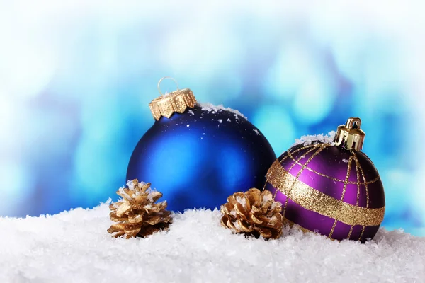 Belle palline di Natale blu e viola e coni nella neve sul retro blu — Foto Stock