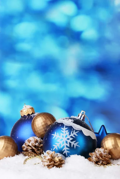 Beautiful blue and golden Christmas balls and cones in snow on blue backgro — Stock Photo, Image